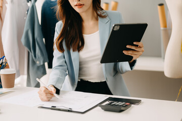 Asian  woman hand using a laptop, smartphone and tablet and writing notebook at the office of her business online shopping. In home with virtual icon .