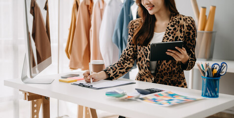 Fashion designer woman talking smart phone and using laptop with digital tablet computer in modern studio.