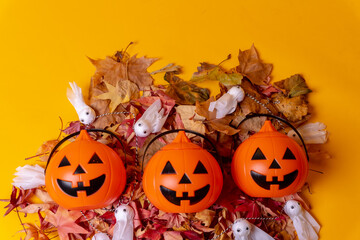 Overhead view of orange Halloween pumpkins on a background of yellow, decorated with red autumn leaves and little ghosts