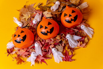 Overhead view of orange Halloween pumpkins on a background of yellow, decorated with red autumn leaves and little ghosts