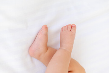 Obraz na płótnie Canvas baby's small feet on a white bed, a place for text, a close-up of a little baby's feet
