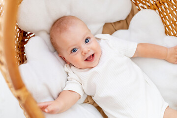 happy joyful baby in a wicker crib smiles or laughs, baby wakes up in the morning or falls asleep,...