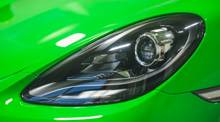 The front headlight of a sporty, modern lime-colored sports car in close-up. Sports car, wrapped in lime-colored film front view. Modern Car exterior details.Headlight of a modern sport car. 