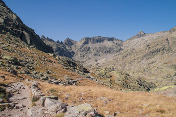 Sendero de la laguna grande en la Sierra de Gredos, Ávila, España. Camino descendete entre hierbas y rocas hasta la laguna y el refugio montañero al pie del pico Almanzor en verano.