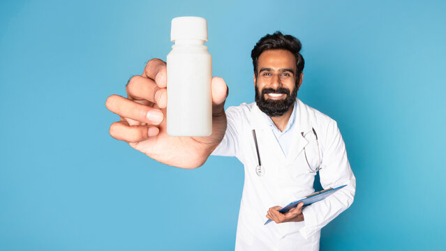 Therapist advice for treatment. Smiling indian man doctor showing jar of medicines on blue background, selective focus