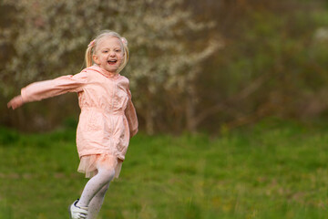 Fototapeta premium Cheerful laughing caucasian girl with blonde hair running across the field. Child girl in the spring in green meadow.