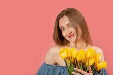 European young woman with blond hair holding bouquet of yellow spring flowers isolated on pink background. Copy space.