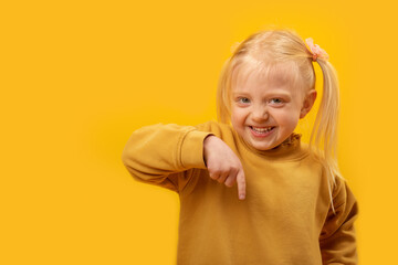 Happy smiling blonde girl with two tails points her finger down. Portrait on yellow background. Copy space.