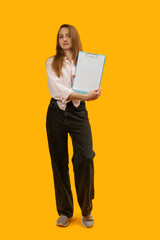 Young woman holding clipboard with documents and looking at camera. Yellow background. Copy space, mock up. Vertical frame