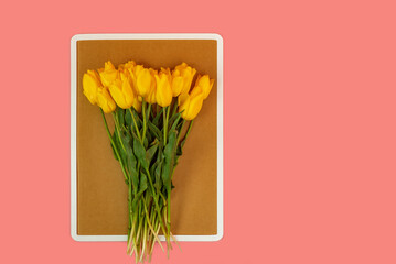 Bouquet of yellow tulips lies on cork board on pink background. Copy space, mock up.