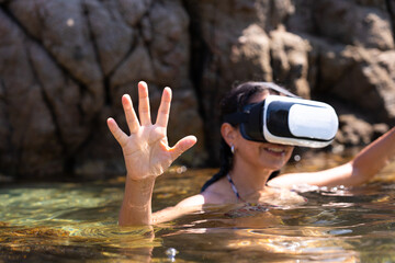 unrecognizable latin woman enjoying a new experience with virtual reality glasses while having a relaxing bath on a beach on the Spanis Costa Brava on a summer day