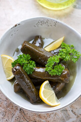 Greek dolmades with fresh parsley and lemon wedges in a grey bowl, vertical shot, middle closeup