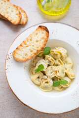 Tortellini in bouillon served with grated parmesan, ciabatta and fresh basil in a beige plate, vertical shot, elevated view