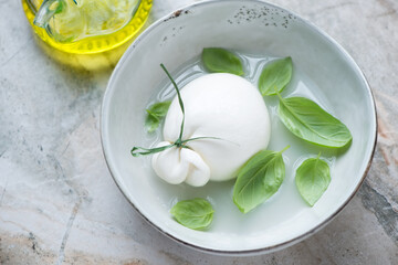 Grey bowl with burrata cheese in brine and fresh green basil, horizontal shot on a grey granite background, selective focus