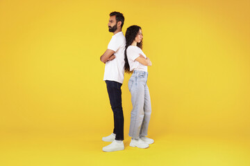 Offended arab young spouses standing back to back, yellow background