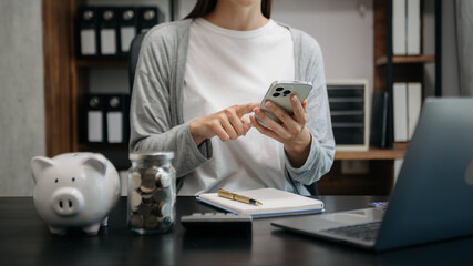 Business woman hand putting money coin into piggy bank with step of growing stack coins for saving...