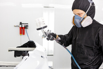 Automotive industry concept. Worker painting car parts in white