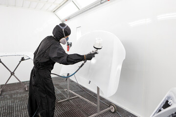 A male master worker paints with a spray gun a part of the car body in white after being damaged at...
