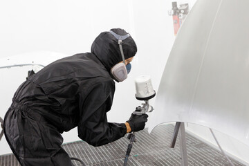 worker painting a car white blank parts in special garage, wearing costume and protective gear