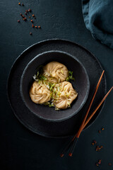 Ready to eat dim sum in the bowl garnished with herbs. Black ceramic textured bowl and plate on the...