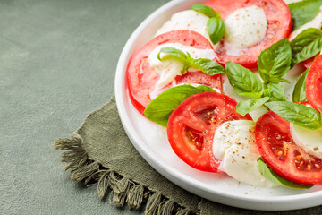 Salad Caprese with tomato, mozzarella and basil on green background. Close up