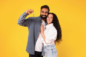 Fototapeta premium Arab Couple Showing New Home Key Hugging On Yellow Background
