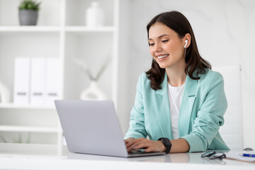 Happy millennial european business lady in wireless headphones use computer to chat