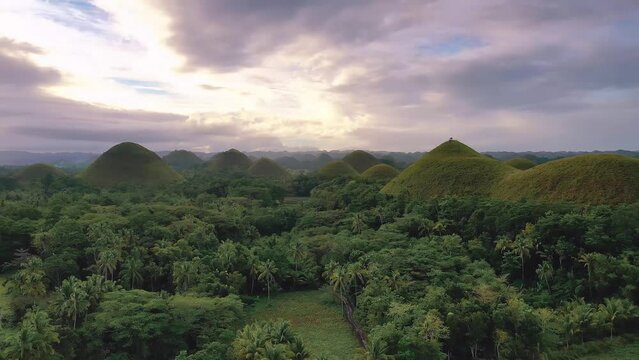Chocolate Hills at sunset in Bohol Island, Philippines. Aerial drone cinematic shot. Low altitude slowly travelling close to hills. Famous landmark. Vibrant dusk colors and dramatic cloudy sunset.