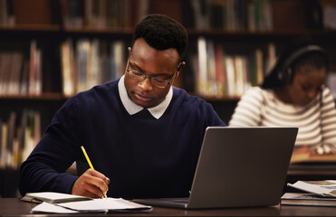 Student, man and writing in library for studying, research and planning in university, scholarship and education. African person with online test and computer for language, e learning or philosophy - obrazy, fototapety, plakaty