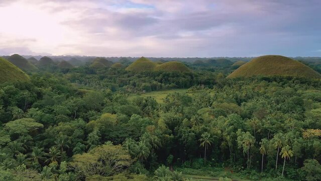 Chocolate Hills at sunset in Bohol Island, Philippines. Aerial drone cinematic shot. Low altitude travelling close to hills. Famous tourist landmark. Vibrant dusk colors and dramatic cloudy sunset.