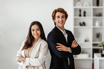 Partnership concept. Successful european man and latin woman standing with arms crossed and smiling, office interior