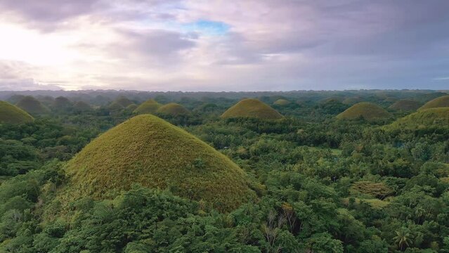 Chocolate Hills at sunset in Bohol Island, Philippines. Aerial drone cinematic shot. Slow upwards travelling above hills. Famous tourist landmark. Vibrant dusk colors and dramatic cloudy sunset.