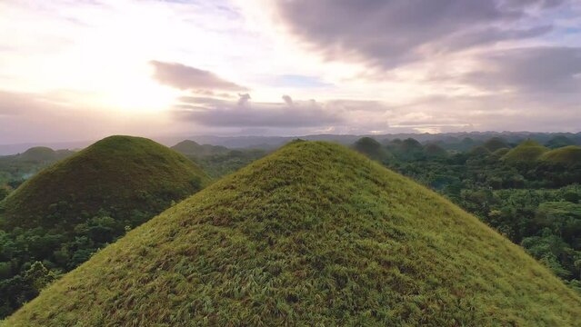 Chocolate Hills at sunset in Bohol Island, Philippines. Aerial drone cinematic shot. Orbit backward travelling close to hills. Famous tourist landmark. Vibrant dusk colors and dramatic cloudy sunset.