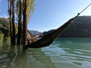 Arm of an unrecognisable person hidden in a hammock over a lake pointing to the right with her...
