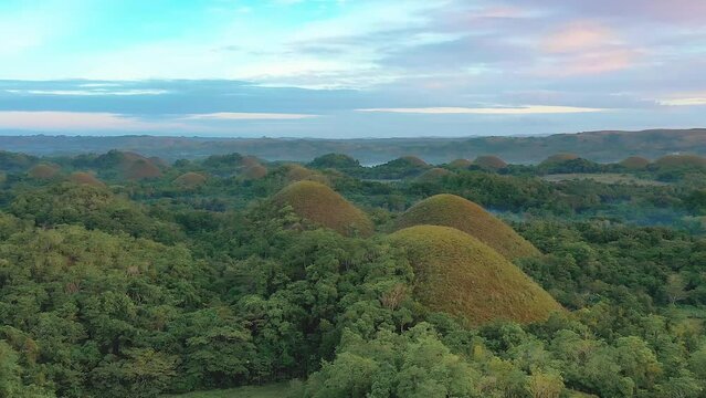 Chocolate Hills at sunset in Bohol Island, Philippines. Aerial drone cinematic shot. Backward travelling from low to high altitude. Vibrant dusk colors and dramatic cloudy sunset.