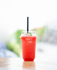 watermelon smoothie, refreshing, in plastic glass, with straw, red Bright, juicy summer drink, on wooden table, nature background.