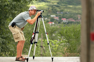 a tall young man of white race, a civil engineer on a construction site, looks into the optical glass of a laser measuring device that calculates the dimensions