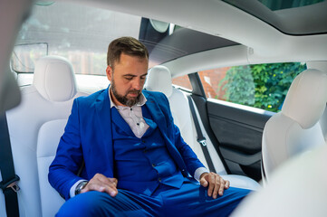 Caucasian man in a blue suit looks asleep in the back seat of a car. Business class passenger. 