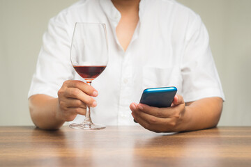 Close-up of hands holding a glass of red wine and a smartphone while sitting at the table.