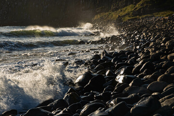 Boulders at Dunstanburgh beach are bathed in the incoming tide at sunrise