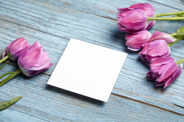 Blank invitation card mockup, white square greeting card with purple flower on blue wooden...