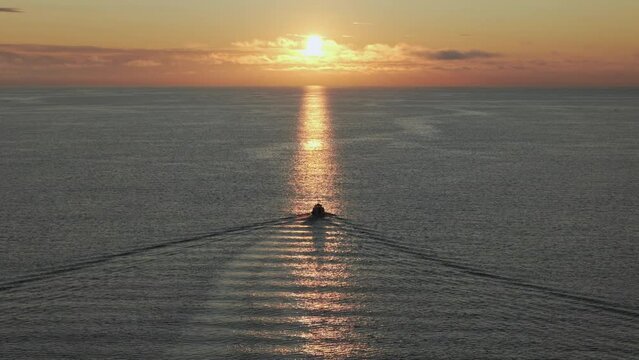 Vessel crossing path of sunlight moving away from camera at dawn, sunrise, glitter path.