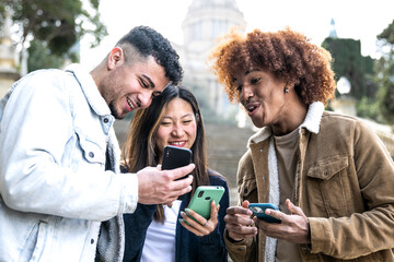 Fototapeta premium Three young diverse people looking at a smartphone and laughing .Multiracial group having fun and using phones in a park.