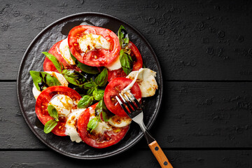 Salad Caprese with tomato, mozzarella and basil on dark wooden background. Italian cuisine concept. Copy space