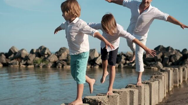 Father and children stand on one leg and balance while playing on the sea coast.