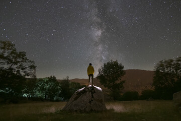 rear view of man climbed on a rock looking at the milky way at night
