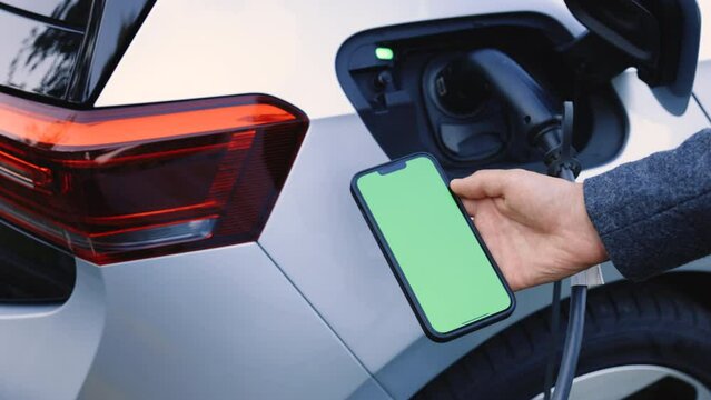Close up green screen mock up chroma key on mobile phone. Male charges batteries, uses phone with chromakey display for activates start charging. EV charging station for electric car with mobile app