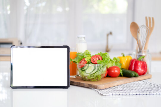 Digital tablet computer with mockup white screen on vegetarian healthy food vegetable background. Online grocery shopping delivery app ads concept, cook book diet plan nutrition recipes, close up view
