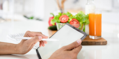 Close up hands holding pen pointing tablet in kitchen.Learn cooking online. woman is taking note in the kitchen.Reading recipe while making deit food Following Recipe On Digital Tablet.