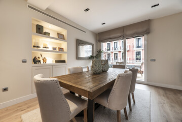 A large wooden dining table flanked by pale fabric upholstered chairs in a living room